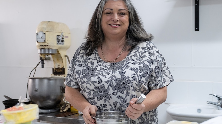 Sarah Schmidt stands behind a kitchen bench whisking cake batter in a bowl