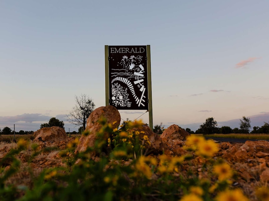 A metal carved sign reads Emerald. Boulders and sunflowers in foreground. Sunset sky in background.