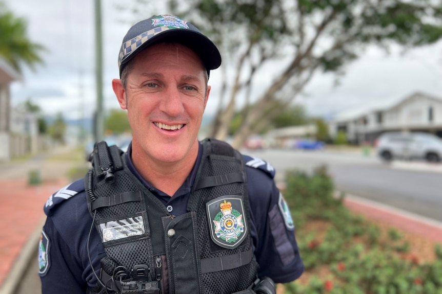 A portrait of a male police officer in uniform beside a residential street.