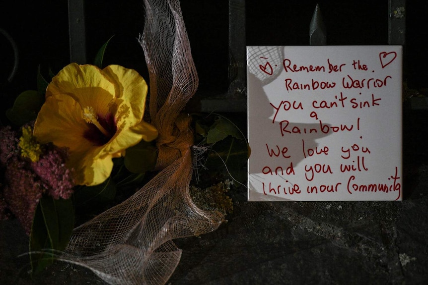 A yellow flower and a sign saying 'remember the rainbow warrior you can't sink a rainbow!'