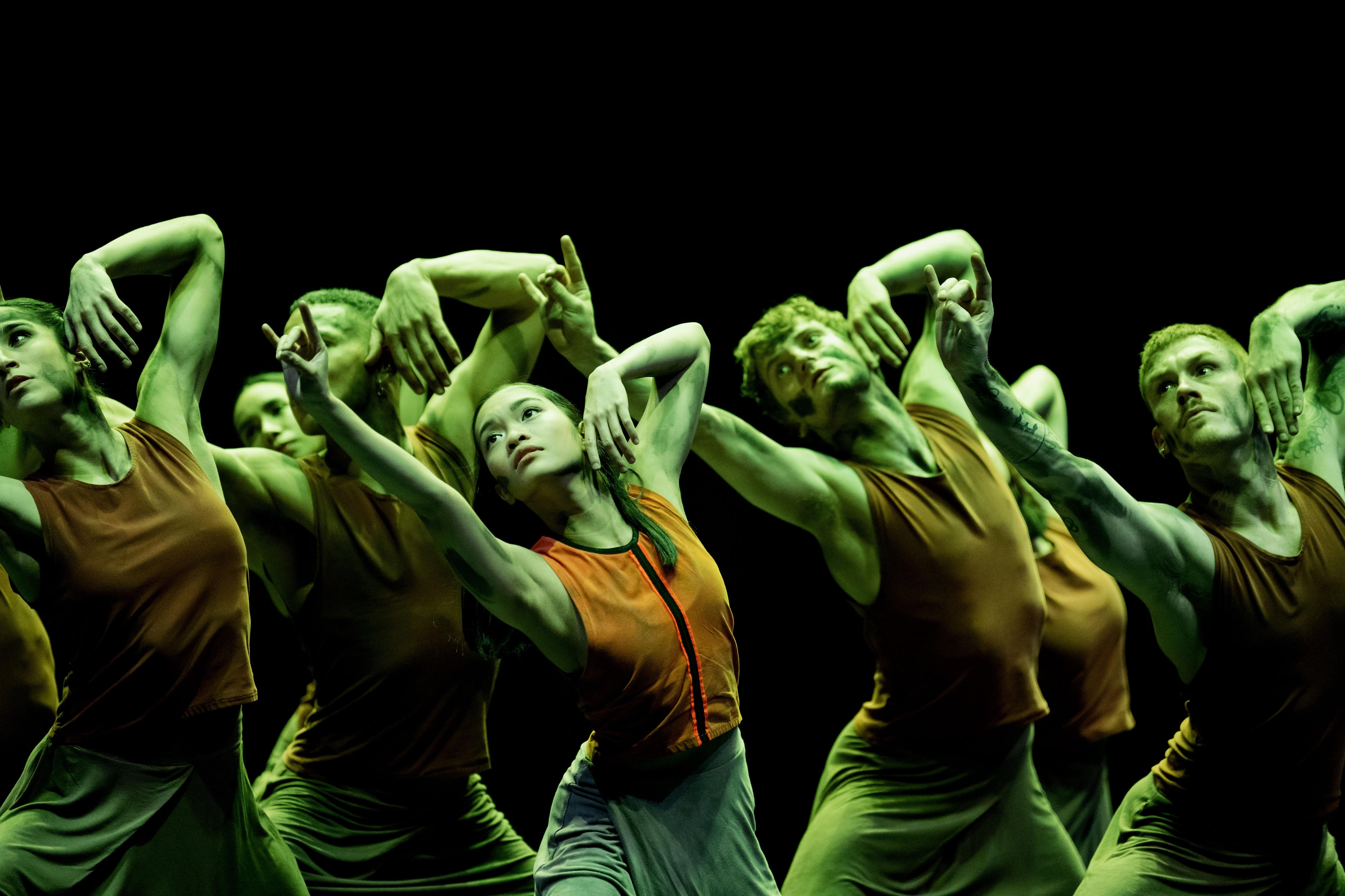 Dancers move together in green light on a stage.