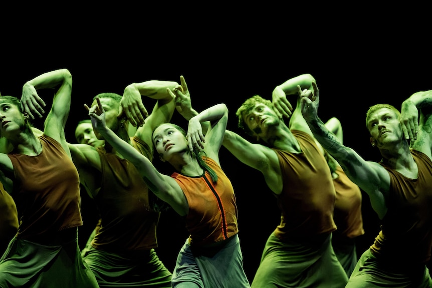 Dancers move together in green light on a stage.