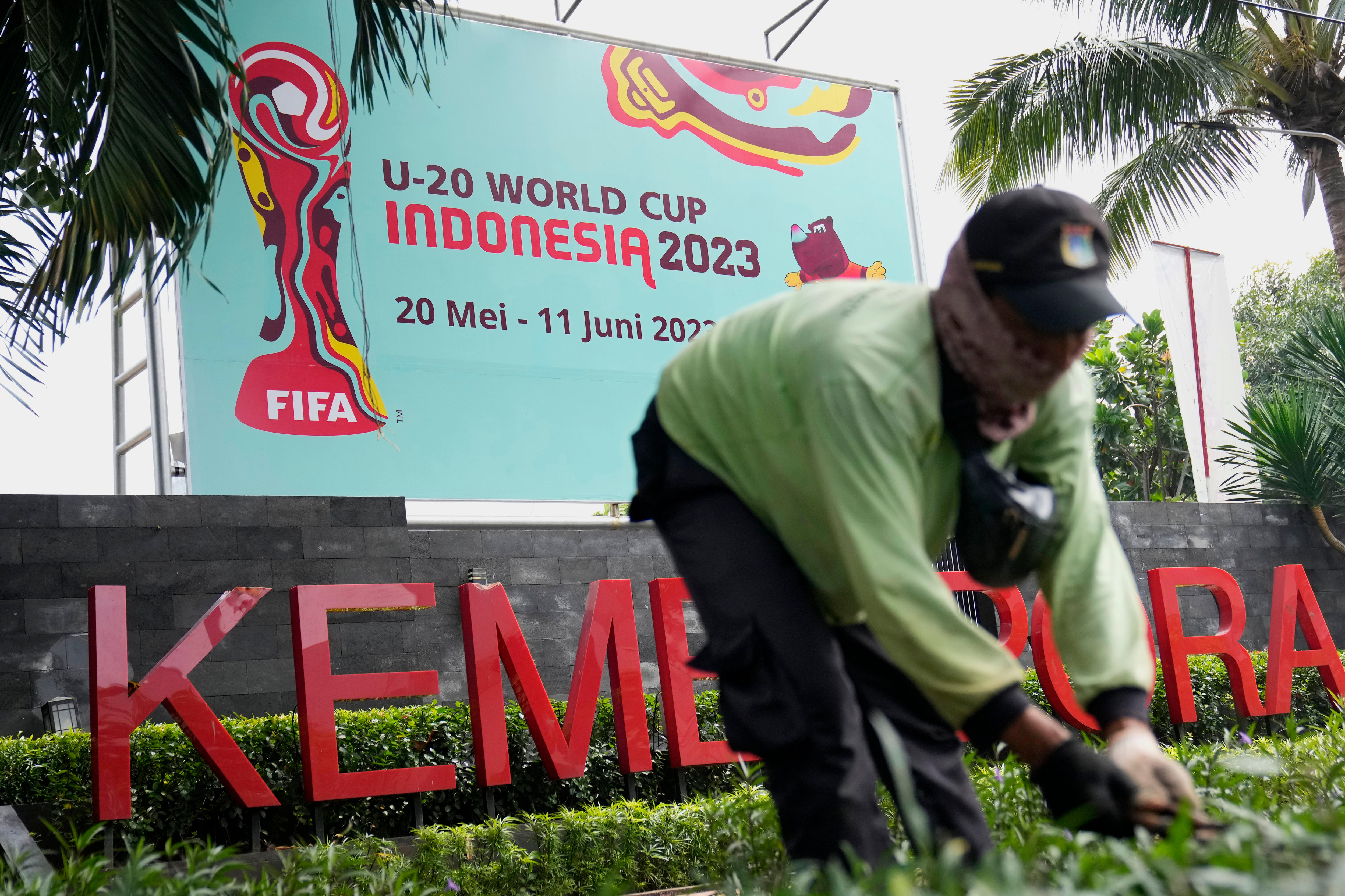 A worker cuts grass near a FIFA U-20 World Cup banner at the Ministry of Youth and Sports in Jakarta.