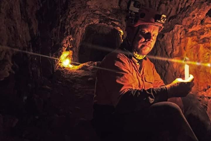 a man holds a candle in an underground mine.