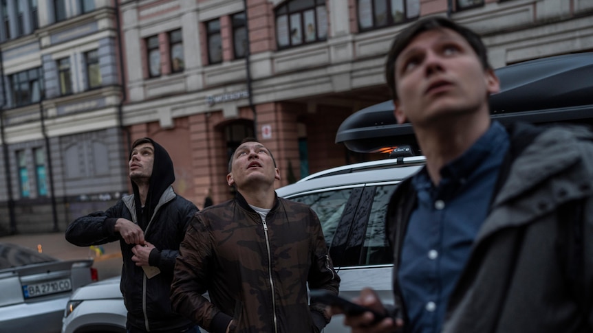 Three men look up towards the sky with mildly concerned expressions on their faces