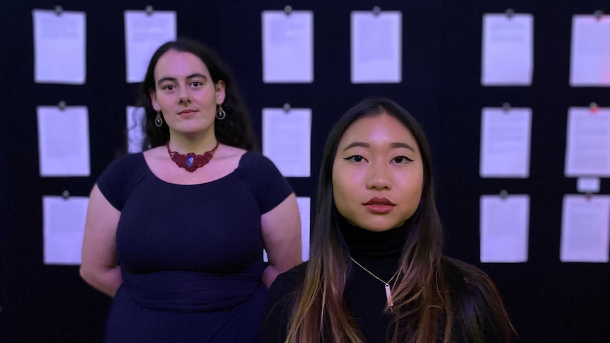 Two women stand in front of a wall of letters that detail the accounts of sexual violence against women