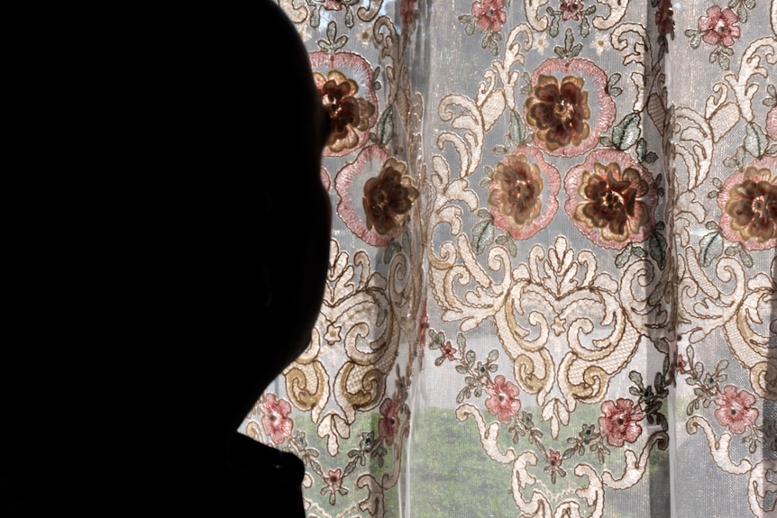 Silhouette of a man from behind looking through an embroidered curtains