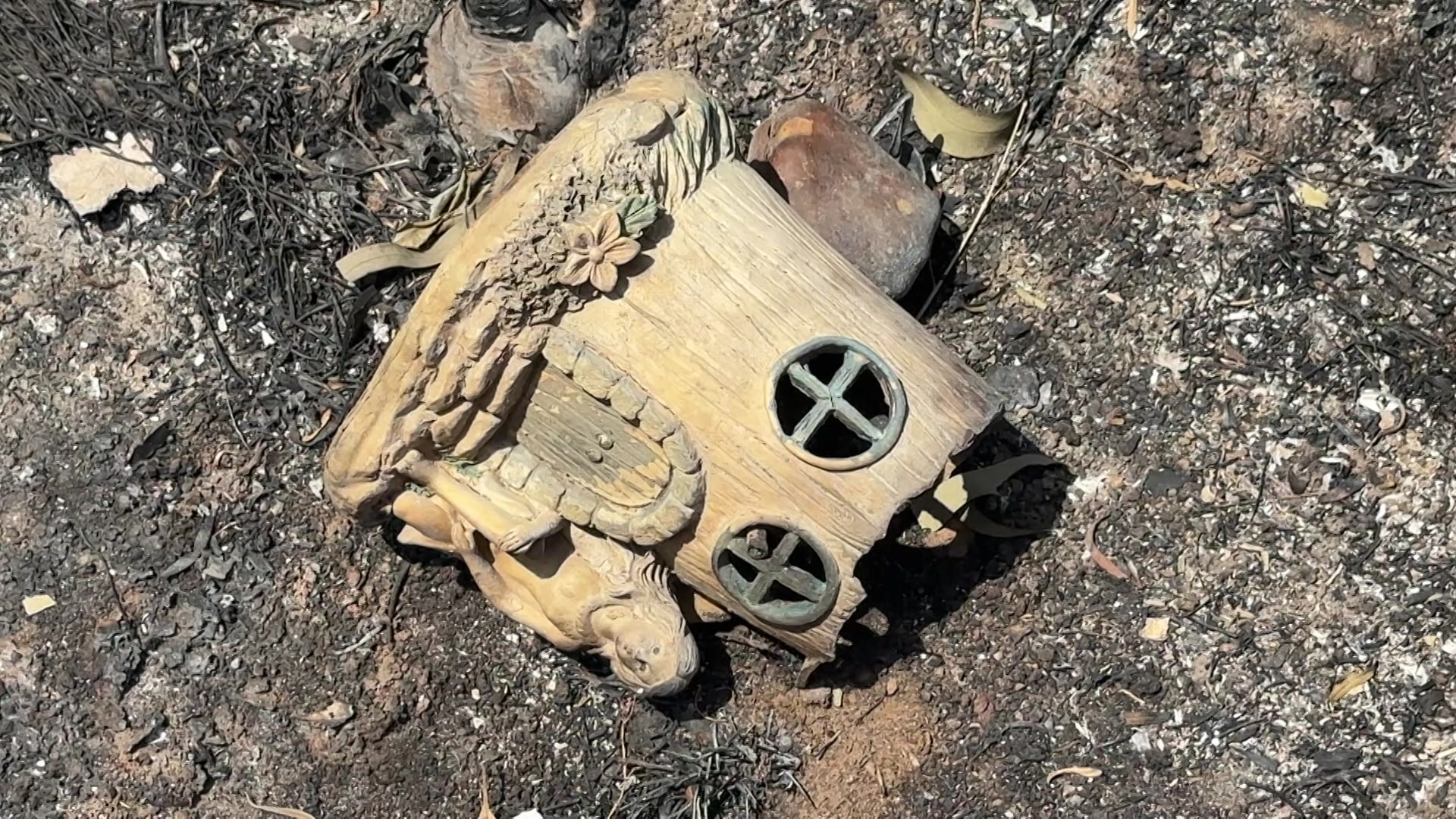 Primer plano de un hada dañada por el fuego y una estatua de árbol sentada en cenizas.