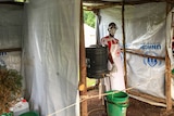 A health worker wears a mask and apron and walks into a makeshift health clinic to pour water