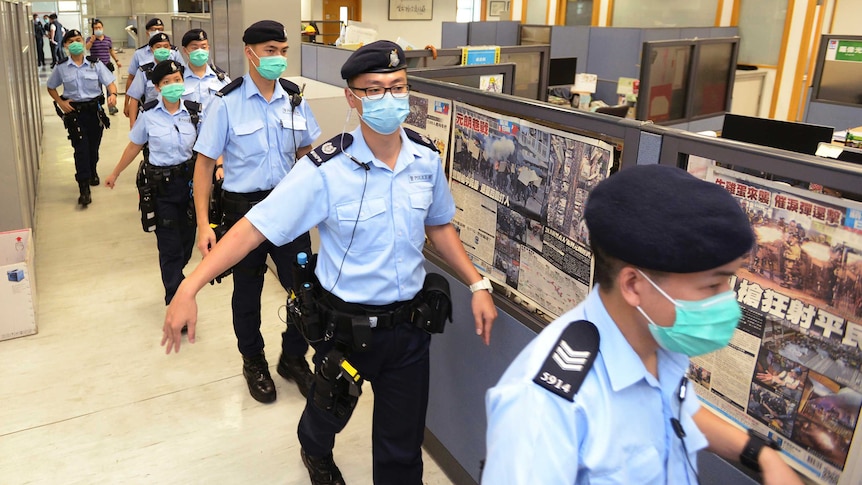 Eight uniformed police wearing face masks walk in a line through a newsroom