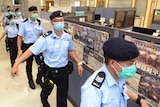 Eight uniformed police wearing face masks walk in a line through a newsroom