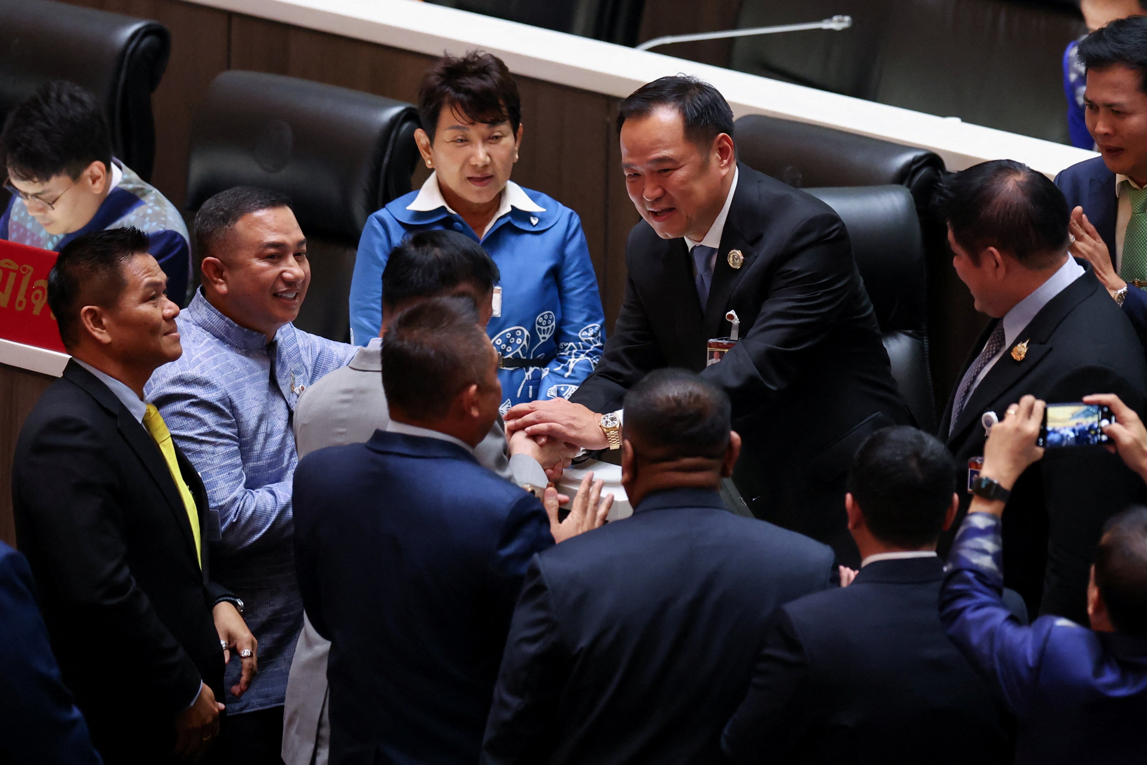 A man shakes the hand of another man as others wait to do the same in a formal room with leather chairs