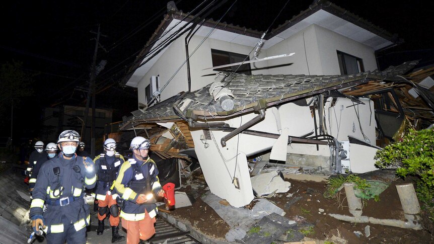 Night time photo of firefighters passing by a collapsed house caused by the earthquake.