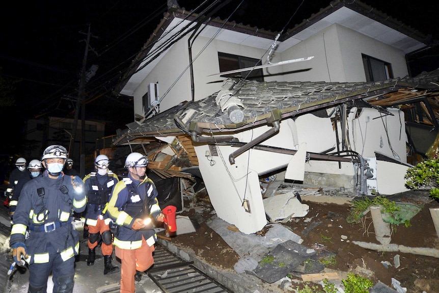 Night time photo of firefighters passing by a collapsed house caused by the earthquake.