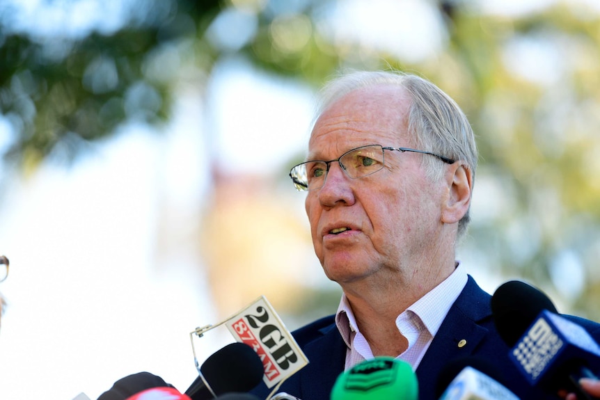 A serious-looking man faces a wall of microphones as he takes part in a press conference.