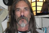 A man with a septum piercing, neck tattoos and long hair looks at the camera.