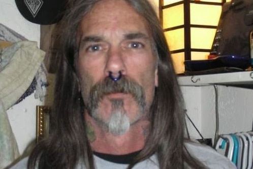 A man with a septum piercing, neck tattoos and long hair looks at the camera.