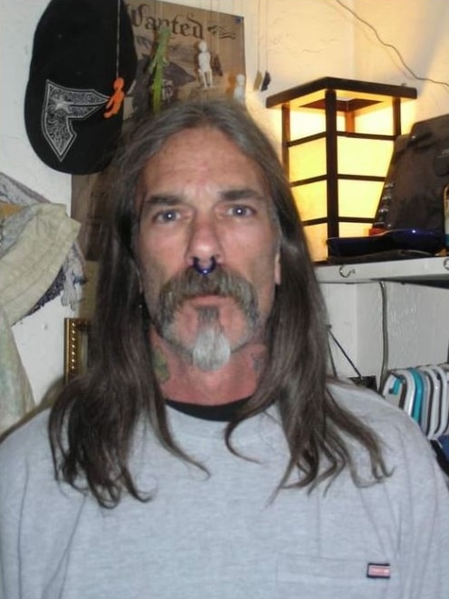 A man with a septum piercing, neck tattoos and long hair looks at the camera.