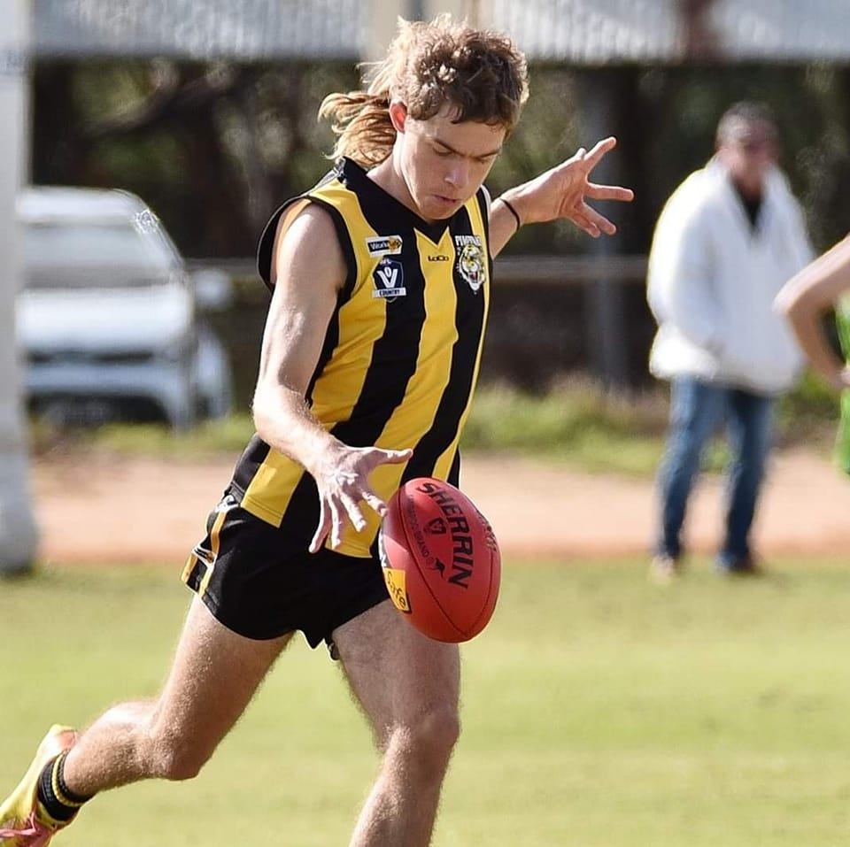 A man in a yellow and black striped shirt with a mullet drops a football 