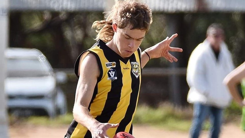 A man in a yellow and black striped shirt with a mullet drops a football 