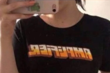 A woman takes a photo in the mirror on her wearing a dark men's t-shirt.