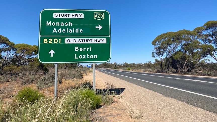 A green sign on the side of a road with a blue sky in the background.