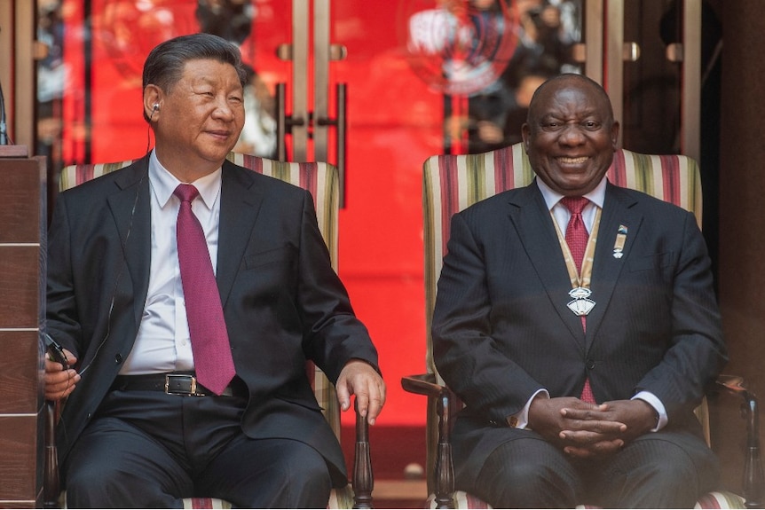 Two men sitting in chairs smiling.