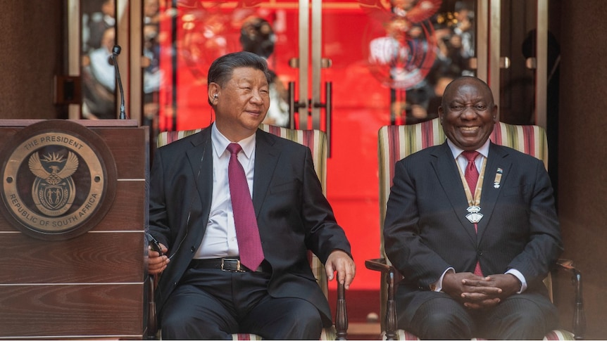 Two men sitting in chairs smiling.