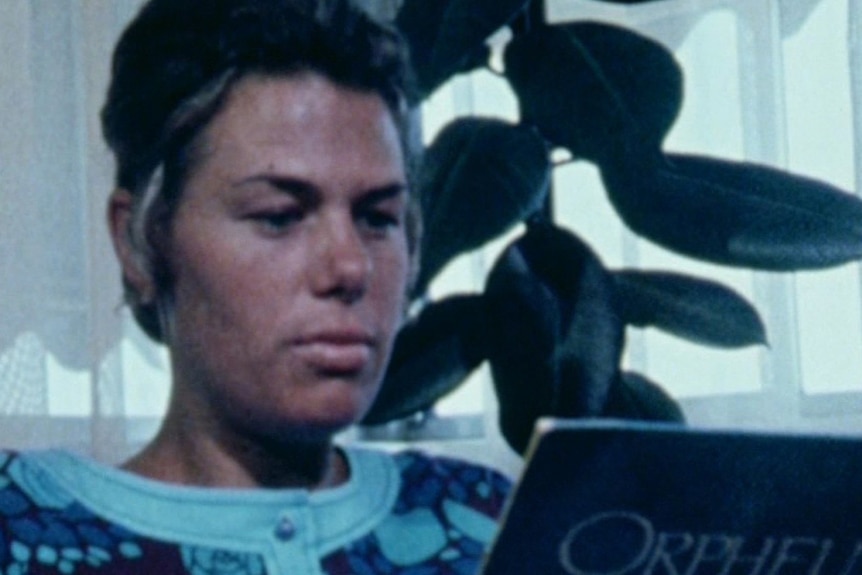 Adrienne Beames sits in a chair looking at a record labelled 'Orpheus'.