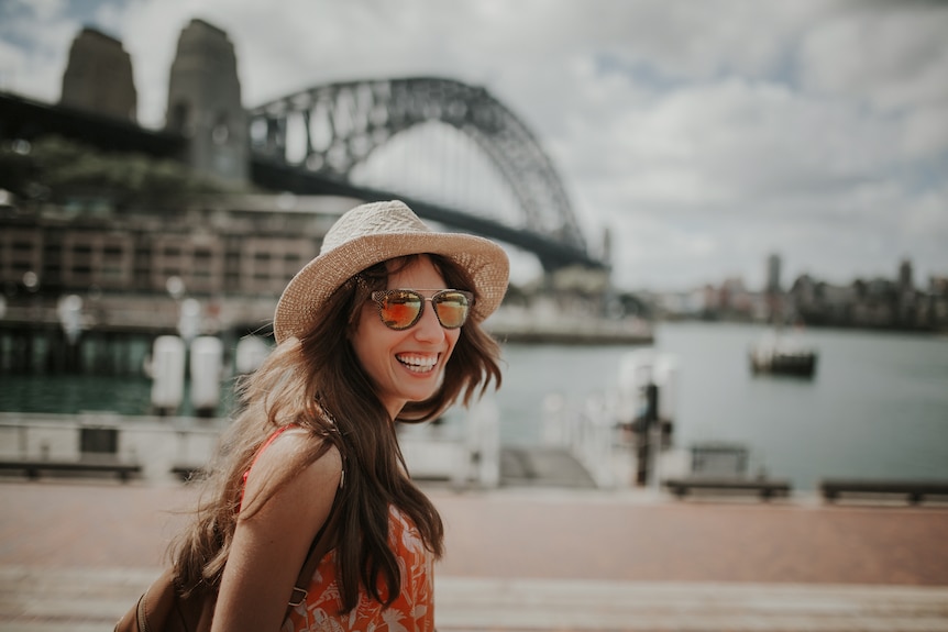 A woman smiling with sungalsses in front of the harbour bridge
