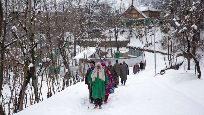 A line of people dressed in heavy clothing walking through thick snow