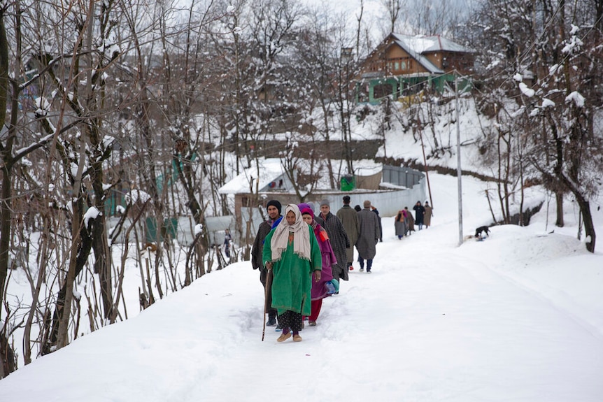 A line of people dressed in heavy clothing walking through thick snow