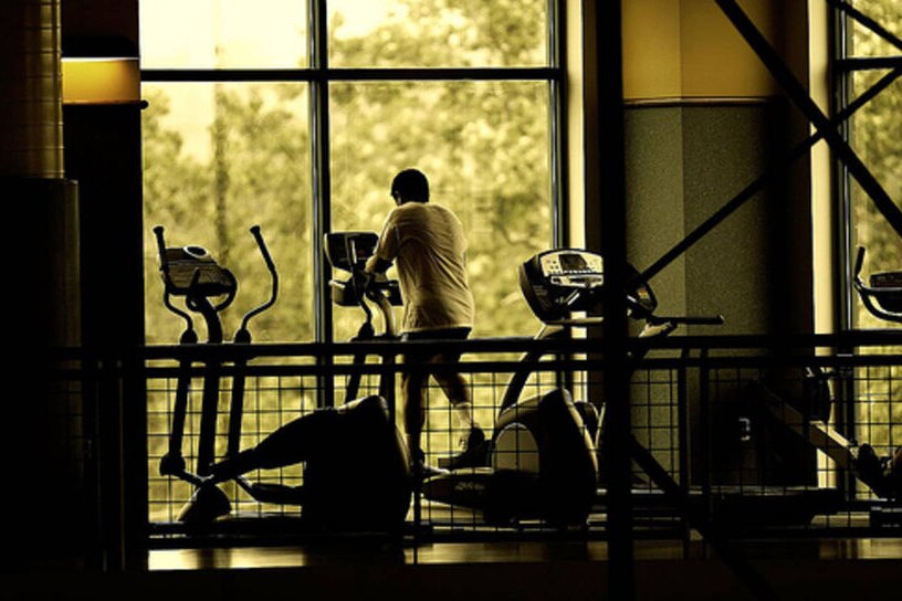 A generic image of a man walking on a treadmill in the gym, in front of a large window.
