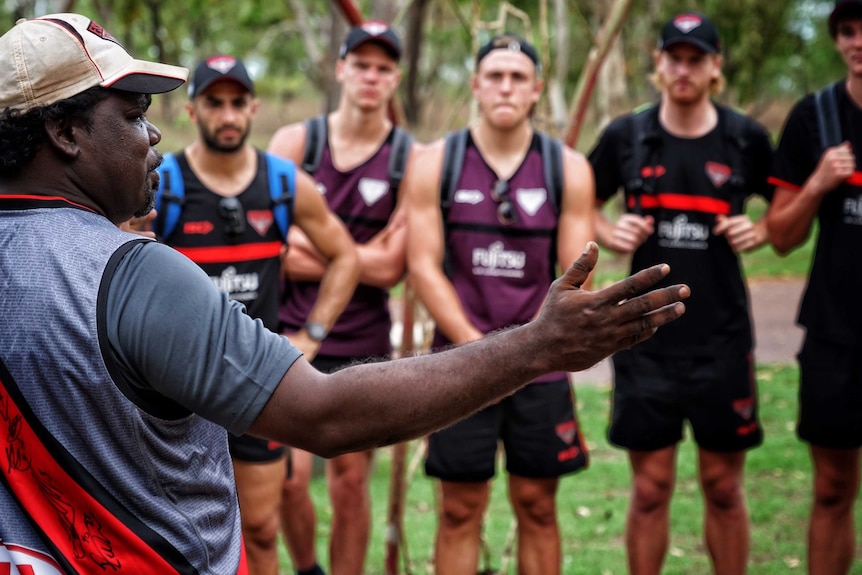 A senior leader gestures with his arm while speaking to Essendon players.