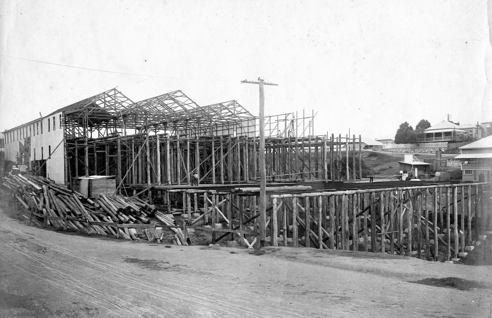 A black and white photo of a half-built timber shed on the side of a hill.