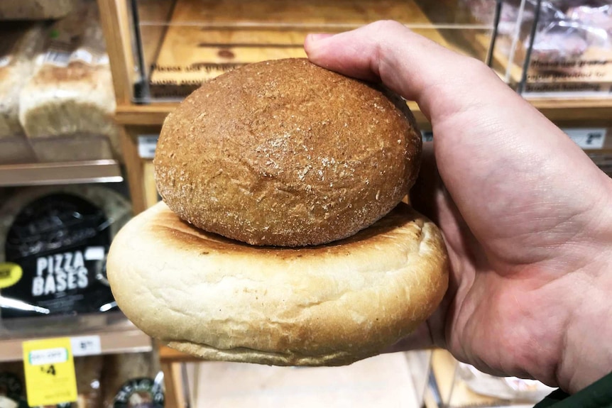 A close-up showing a hand holding two bread rolls representing our reporter's attempt to go one week without plastic.