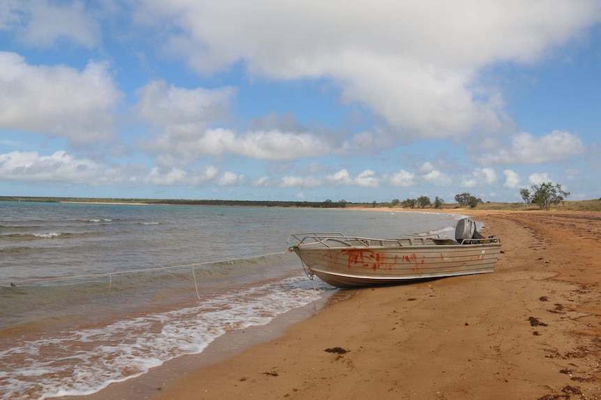 A tinny boat rests on the shore as waves lap up against it.