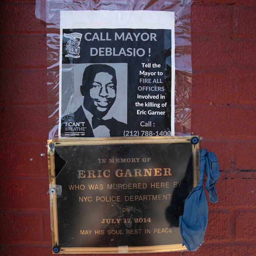 A sign and plaque are mounted on a red wall detailing the killing of Eric Garner at the hands of New York police
