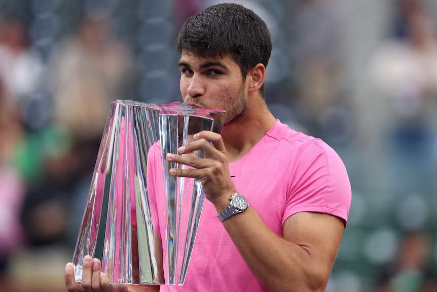 Carlos Alcaraz kisses the men's Indian Wells trophy at the presentation ceremony.