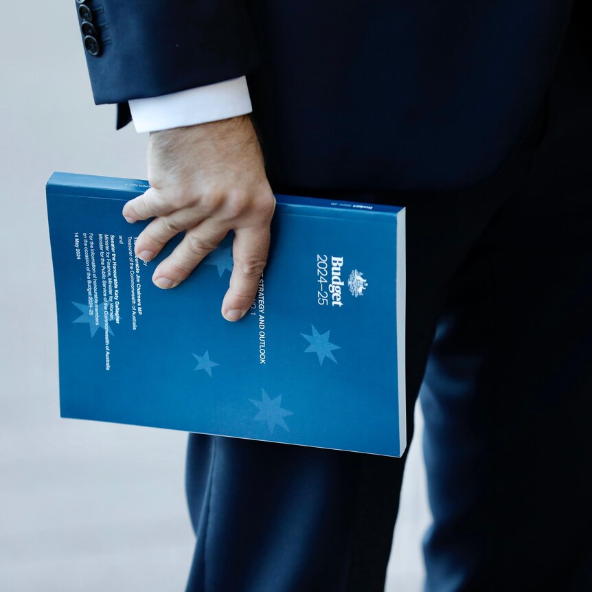  Jim Chalmers holds a copy of the 2024 Budget papers as he arrives at Parliament House
