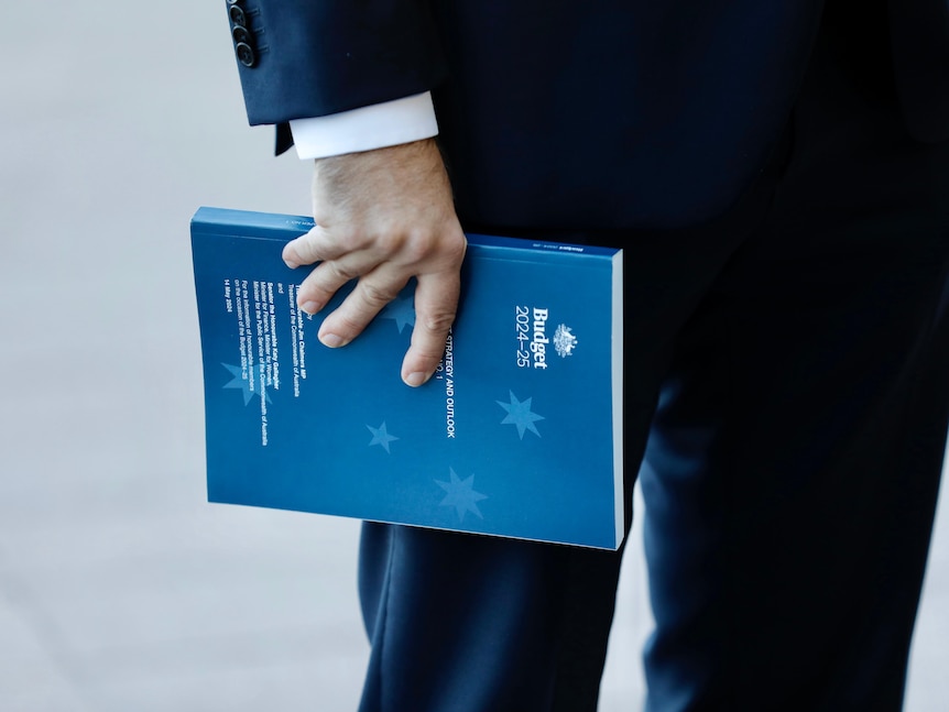 Jim Chalmers holds a copy of the 2024-25 budget outside of Parliament House