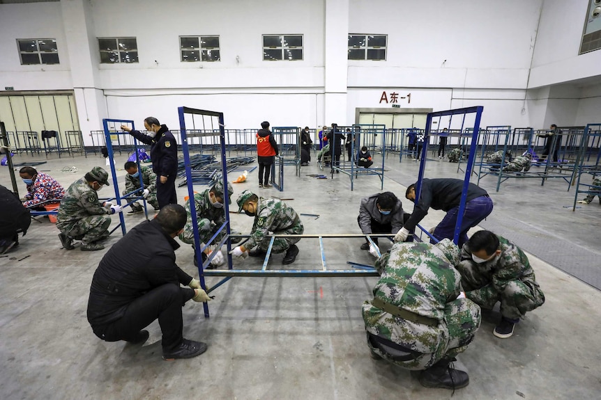 Soldiers and workers build beds in a convention centre.