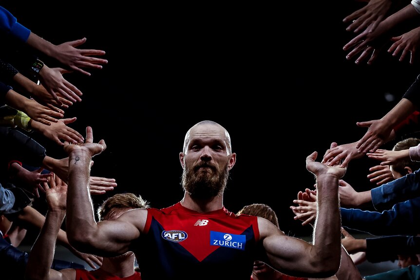 A tall, bald AFL player looks at the camera as he walks down the race after a game, holding his hands out for fans to high-five.