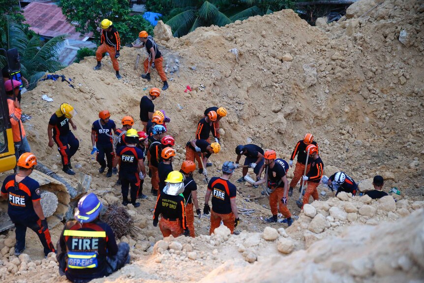 Several rescuers use excavators and pickaxes to move large amounts of earth after landslide.