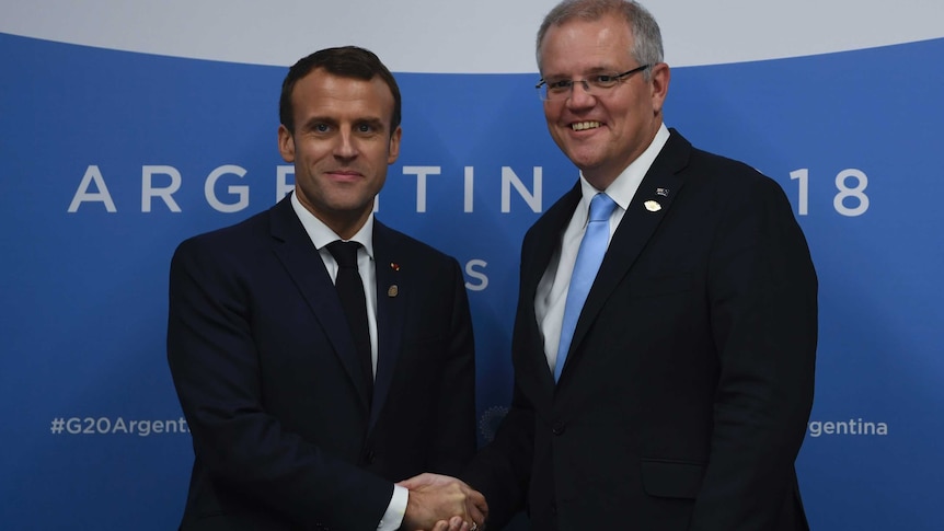 Scott Morrison and Emmanuel Macron smile and shake hands as they pose for a photo.