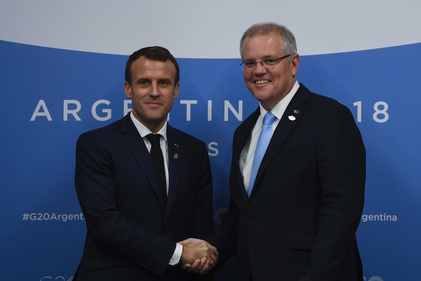 Scott Morrison and Emmanuel Macron smile and shake hands as they pose for a photo.