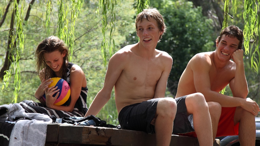 A girl and two boys sit on a platform after swimming in a tropical setting
