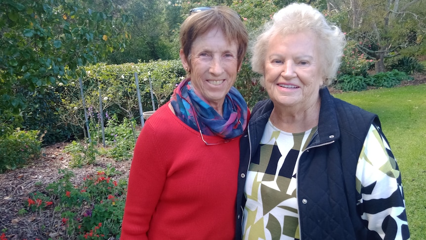 two women standing in a garden smiling at the camera