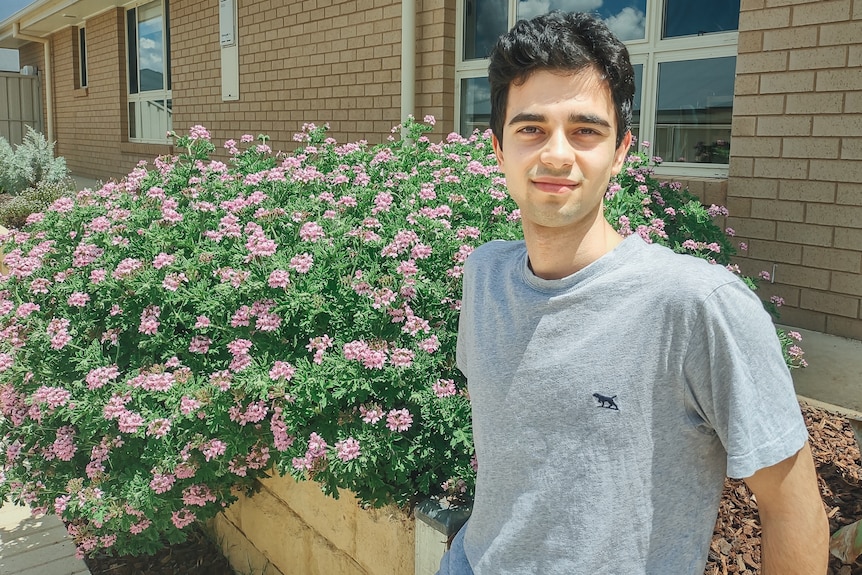 a young man sits on a low brick wall near a flowring shrub