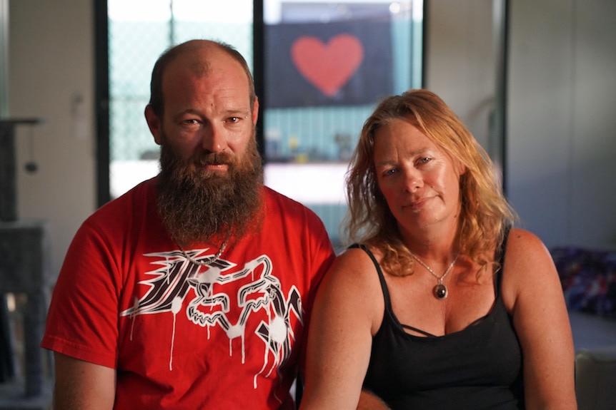 A bearded man wearing a red t-shirt and a woman wearing a black top.